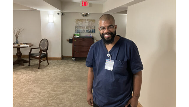 Person in navy scrubs standing in a hallway of a senior living community.